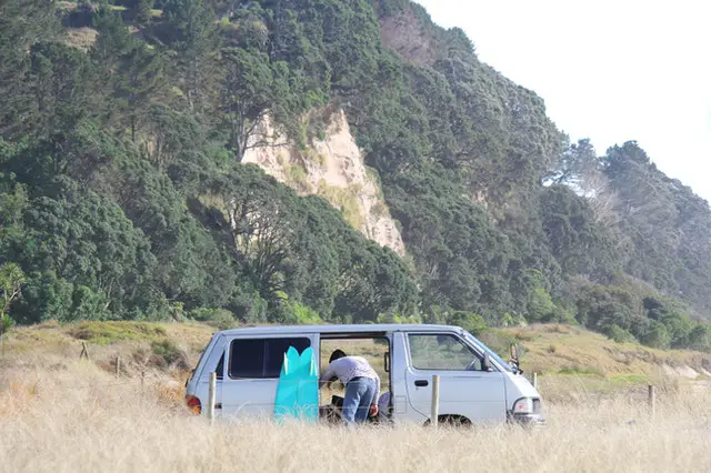 Homme de dos qui cherche quelque chose dans son vieux van gris.